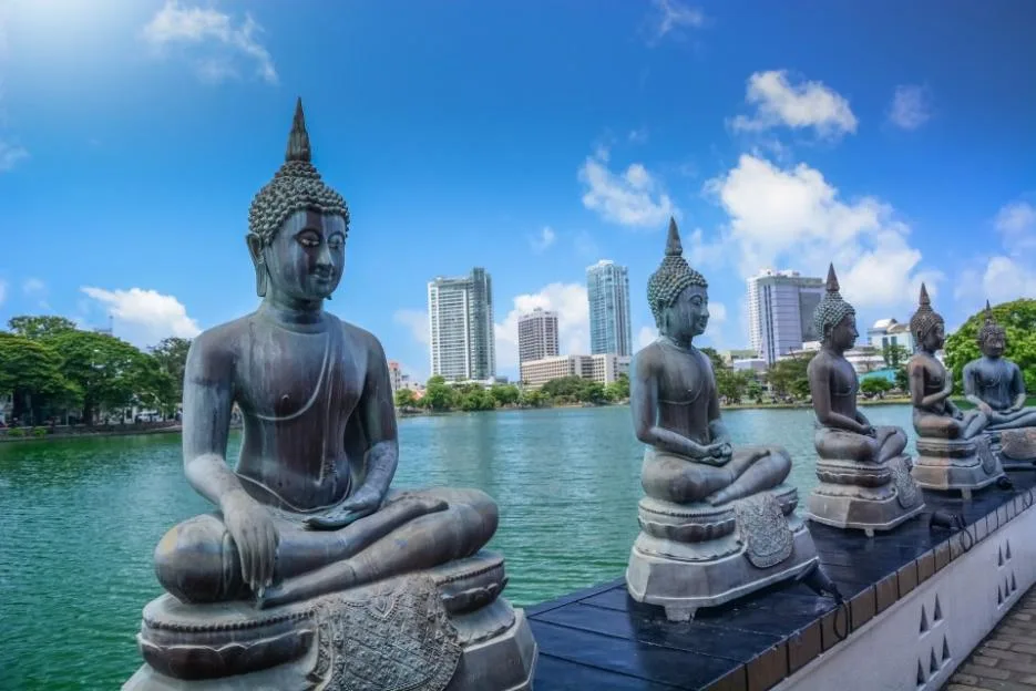 Several Buddha statues at the Seema Malaka Temple overlooking Beira Lake and the Colombo city skyline.