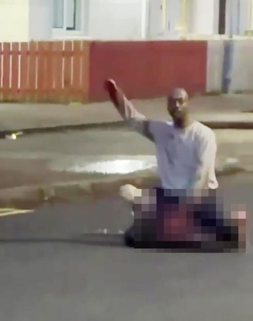 A man with a knife over a prone, pixelated figure on the street.