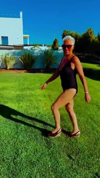 Denise Welch in a black swimsuit and sunglasses walking on green grass in Portugal.