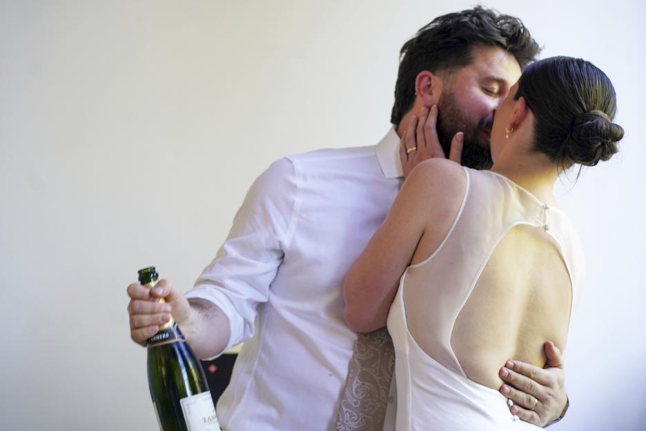 A newly married couple kissing, the groom holding a bottle of champagne.