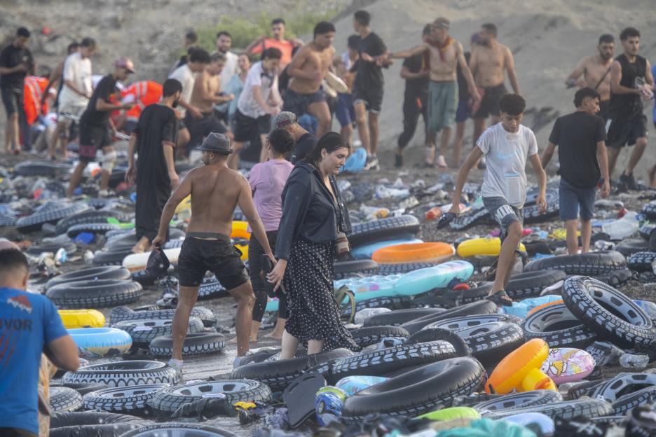 Migrants stand on a beach covered with deflated inflatable rings and inner tubes after swimming from Morocco to Ceuta, Spain.