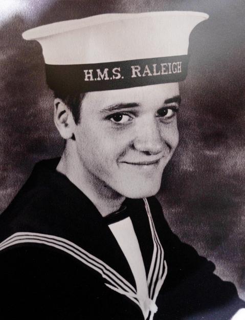 Black and white photo of Simon Parkes in 1985 wearing a "H.M.S. RALEIGH" sailor cap and uniform.
