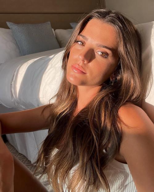 Ines Aguiar with long brown hair, sitting on the floor by a bed, with sunlight highlighting her face and hair.