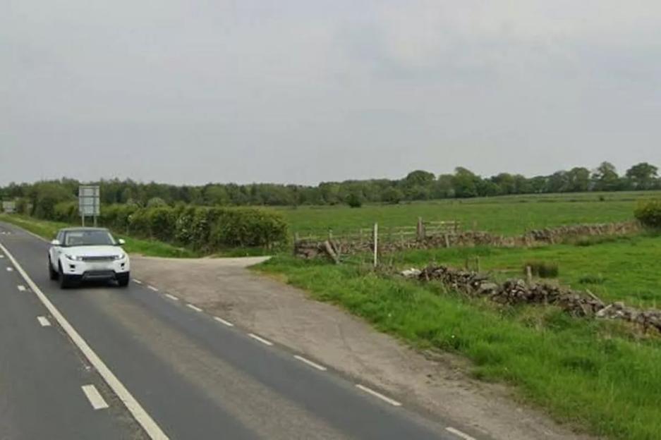 A white Range Rover driving on a highway, with a grassy field and stone wall alongside the road.