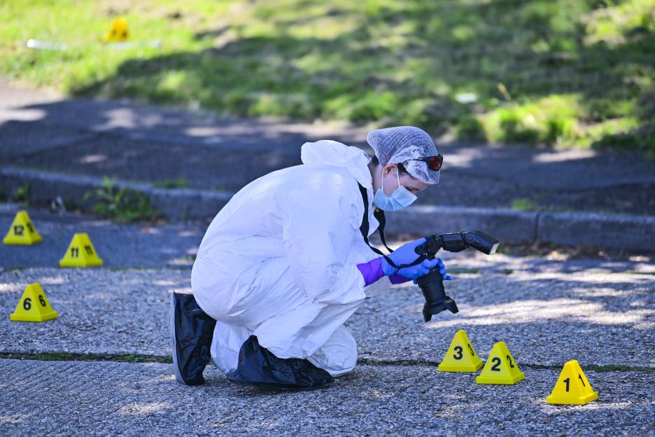 A forensic investigator in a white suit, face mask, and gloves takes a photo at a crime scene.