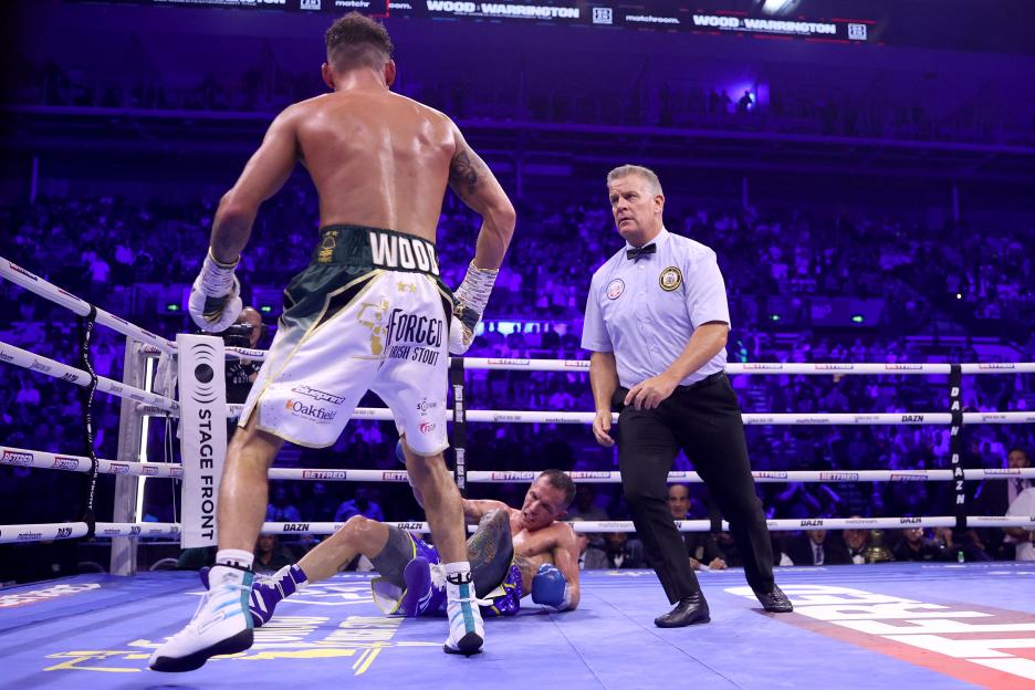 Leigh Wood stands over Josh Warrington, who is down on the canvas, as a referee looks on.