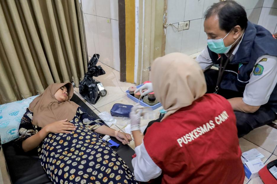 A female student lies on a cot while medical personnel attend to her.