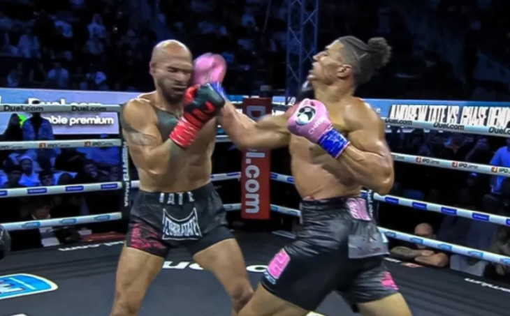Two male boxers, one bald and one with a man bun, punch each other in a boxing ring.