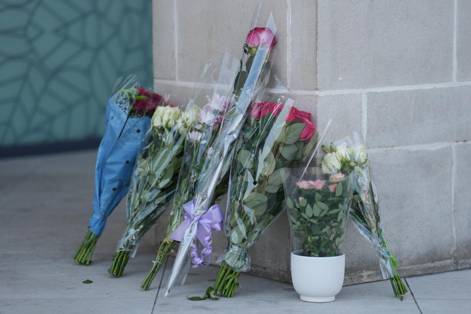 Floral tributes, including wrapped bouquets of roses, left leaning against a stone wall.