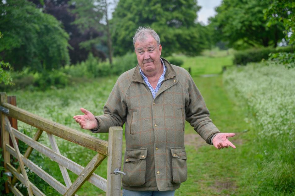 Jeremy Clarkson shrugging in a green field next to a wooden fence.