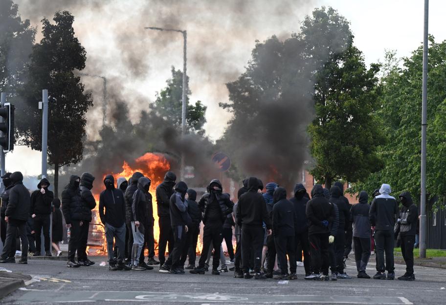 Youths gather in front of a burning barricade, creating thick smoke, during demonstrations in Belfast, Northern Ireland.