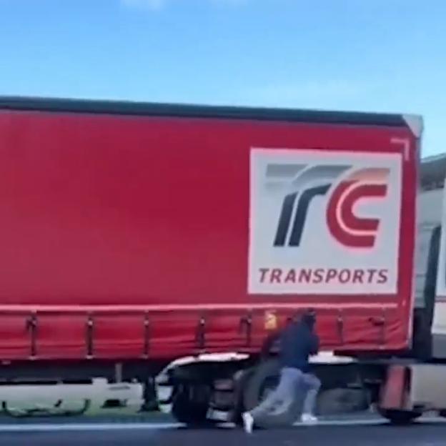 A migrant runs alongside a red "ITC TRANSPORTS" truck.