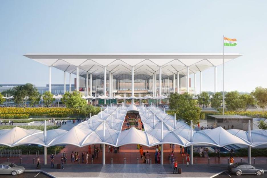 Illustration of a modern, multi-story airport with a large white roof and a long covered walkway leading to the entrance, with an Indian flag flying on the right.