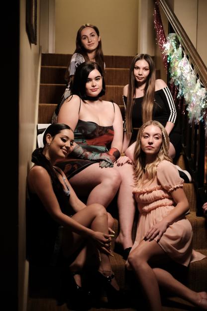 Five young women, dressed in fashionable clothes, pose on a set of stairs decorated with tinsel.
