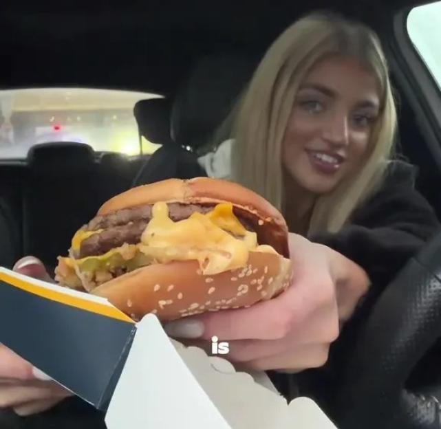 A woman in a car holding a burger from McDonald's.