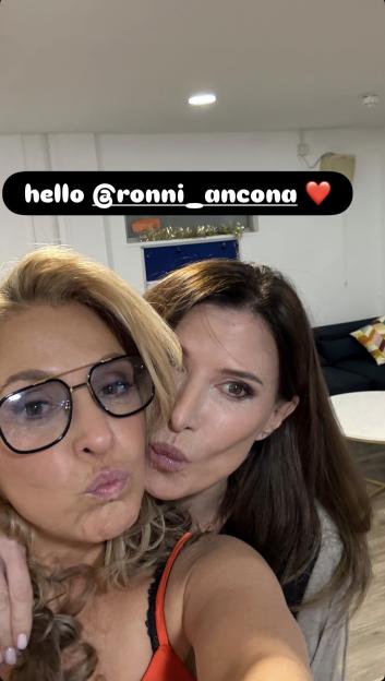 Two women posing for a photo, one in glasses and an orange top, the other in a grey cardigan and black top.