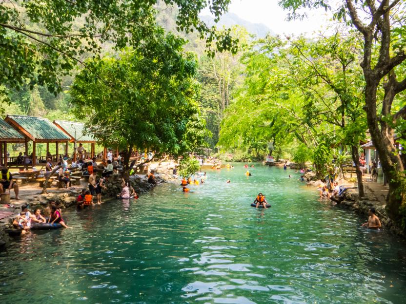 View of the Blue Lagoon 1 in Vang Vieng, Laos, with people swimming and relaxing in the water and on the banks.