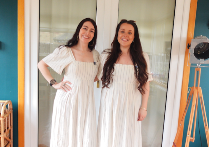 Two women smiling, both wearing matching pinstriped dresses.