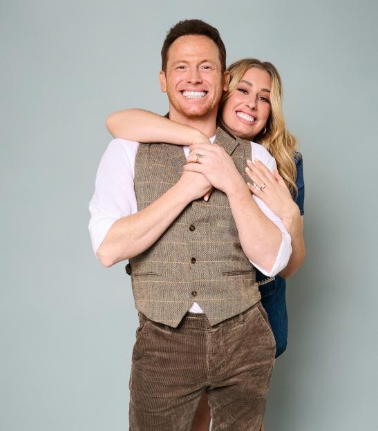 Stacey Solomon and Joe Swash smiling at the camera, with Solomon hugging Swash from behind.