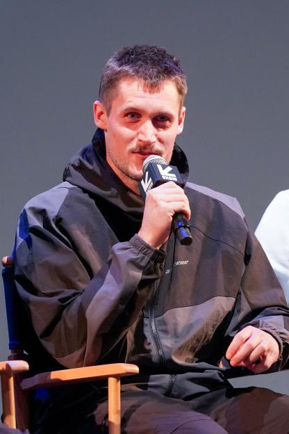 A man with a mustache and a dark jacket speaks into a microphone at the "We Are Storror" Premiere at SXSW.