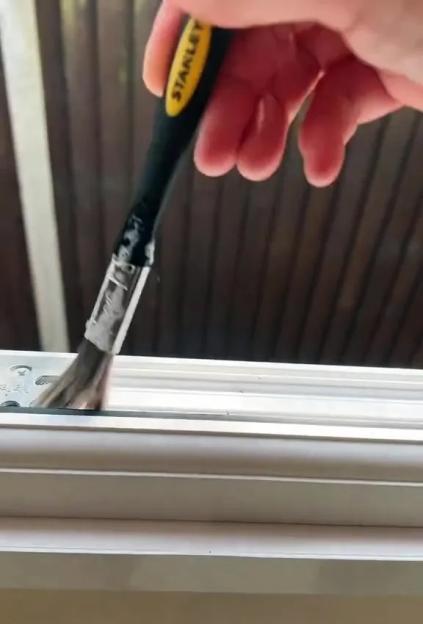 A person using a paint brush to clean dust out of a window track.