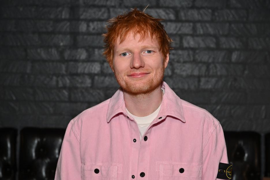 Ed Sheeran wearing a pink corduroy shirt over a white t-shirt.