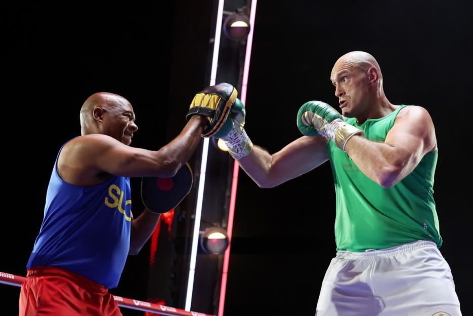 Tyson Fury in a green tank top and white shorts boxing with a trainer.