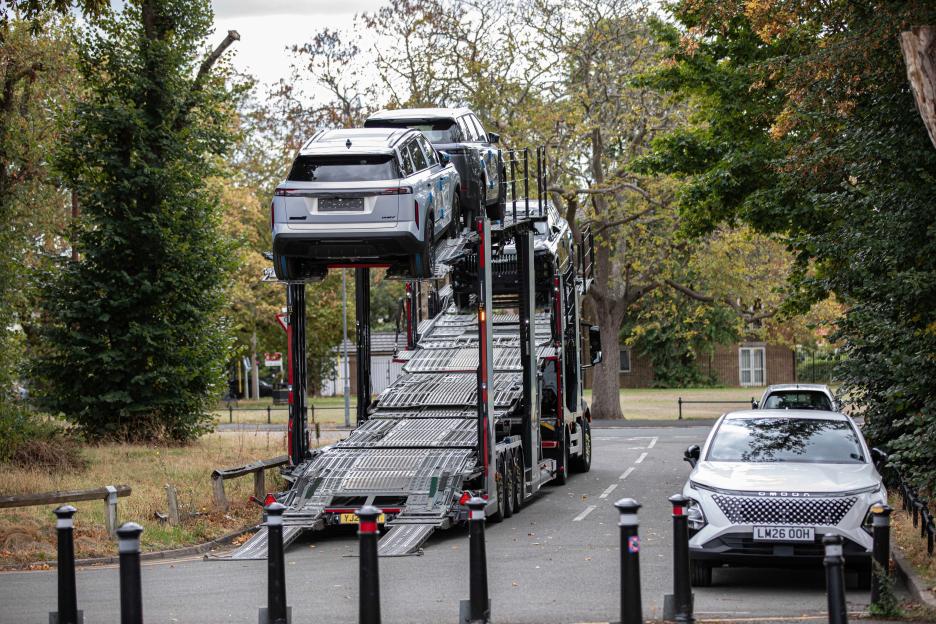 A car carrier truck, partially unloaded, parked on a street with cars on its top and bottom decks.