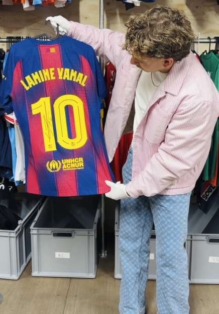 A person wearing white gloves holds up a blue and red soccer jersey with "LAMINE YAMAL" and the number "10" on the back.