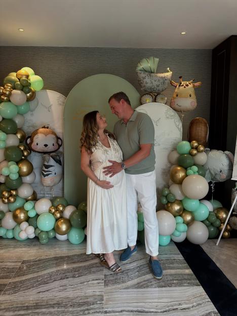 Zara Holland and her partner posing in front of balloons and decorations, with her baby bump visible.