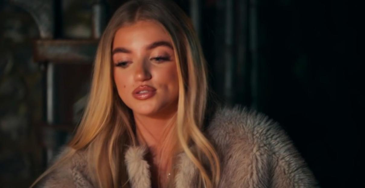 Princess Andre, with long blonde hair, looking down while wearing a light brown fur coat.