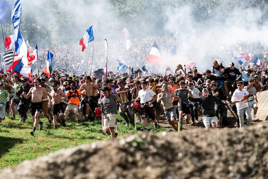 A large crowd of spectators running along the UCI Mountain Bike World Series course, with French flags visible.