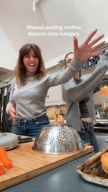 Two women dancing in a kitchen, with a text overlay that reads: "Always putting mother dearest onto bangers."