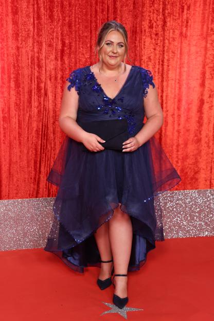 Clair Norris in a navy blue dress with blue sequin embellishments, holding a clutch on a red carpet.