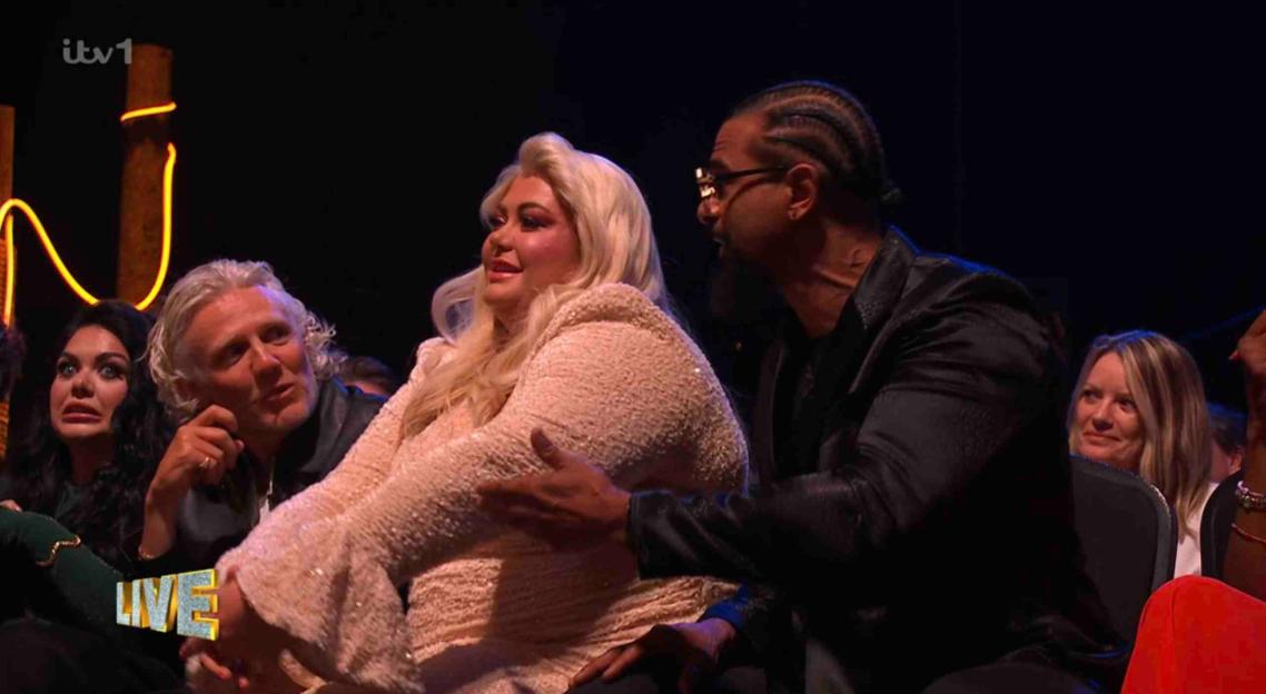 A woman in a peach-colored sequined dress touches another man's arm as a man with long white hair watches.