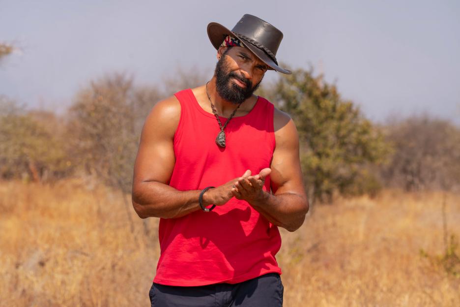 David Haye from "I'm a Celebrity... South Africa" in a red tank top and brown hat, standing outdoors.
