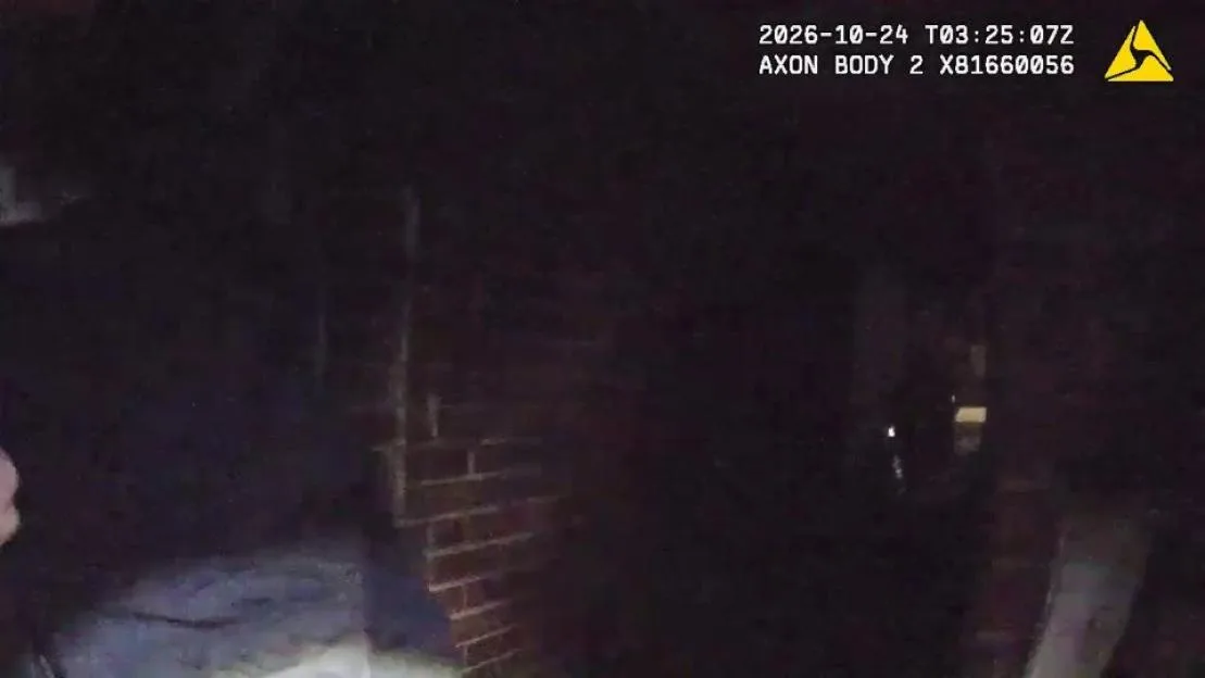 Police body-worn camera footage showing a dark outdoor scene with a brick wall illuminated by a flashlight.
