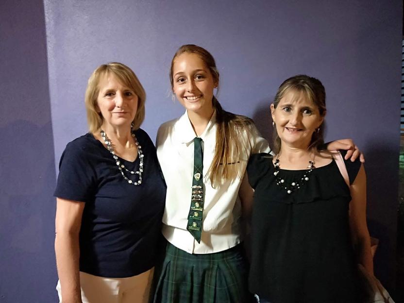 Three females standing side by side, a young girl in school uniform between two older women.