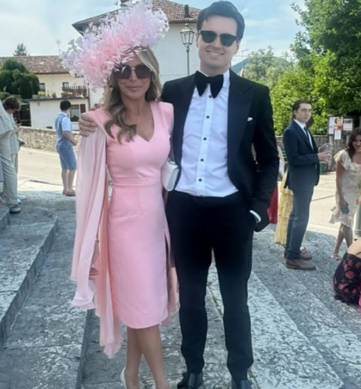A woman in a pink dress and feathered hat standing next to a man in a tuxedo.