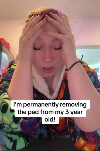 A woman with red-patterned nails holds her head in her hands while wearing a colorful bathrobe. Text reads, 'I'm permanently removing the pad from my 3-year-old!'