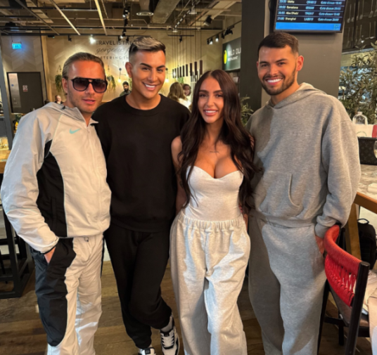 Four people smiling and posing for a photo in what appears to be an airport lounge.