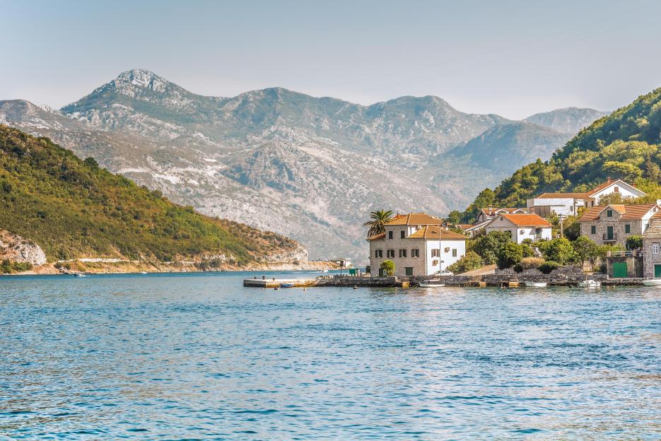 View of the coast from a ferry in Lepetane, Tivat, Montenegro, showing houses, mountains, and the sea.