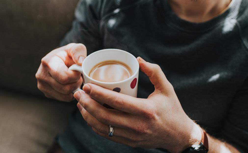 Man holding a steaming cup of tea with both hands.