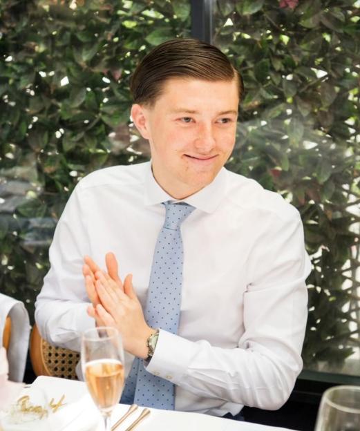 Henry Nowak, a university student, is pictured at a table with a drink, clapping his hands.