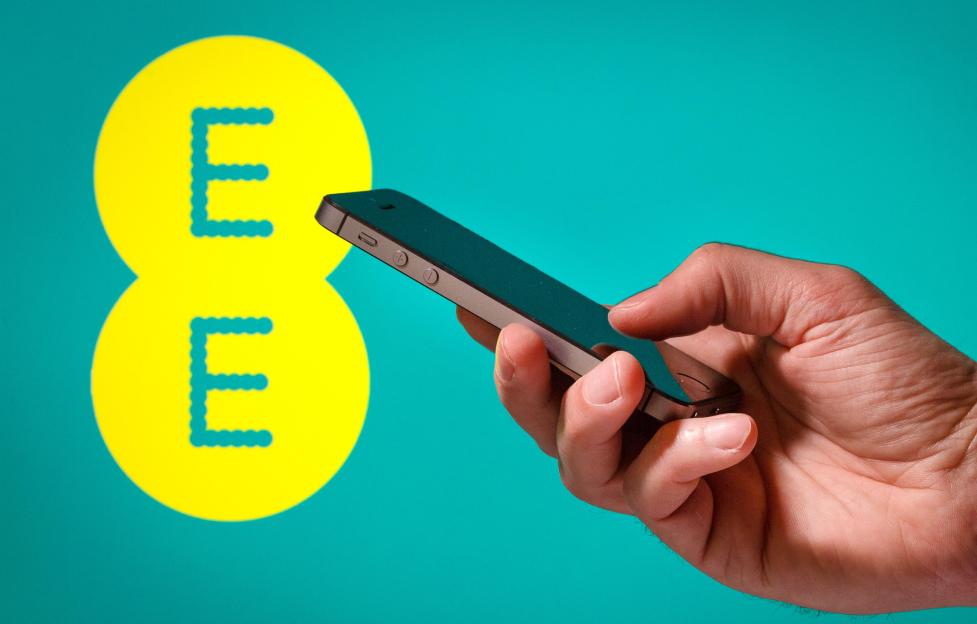 A hand holding a mobile phone in front of an EE network logo.