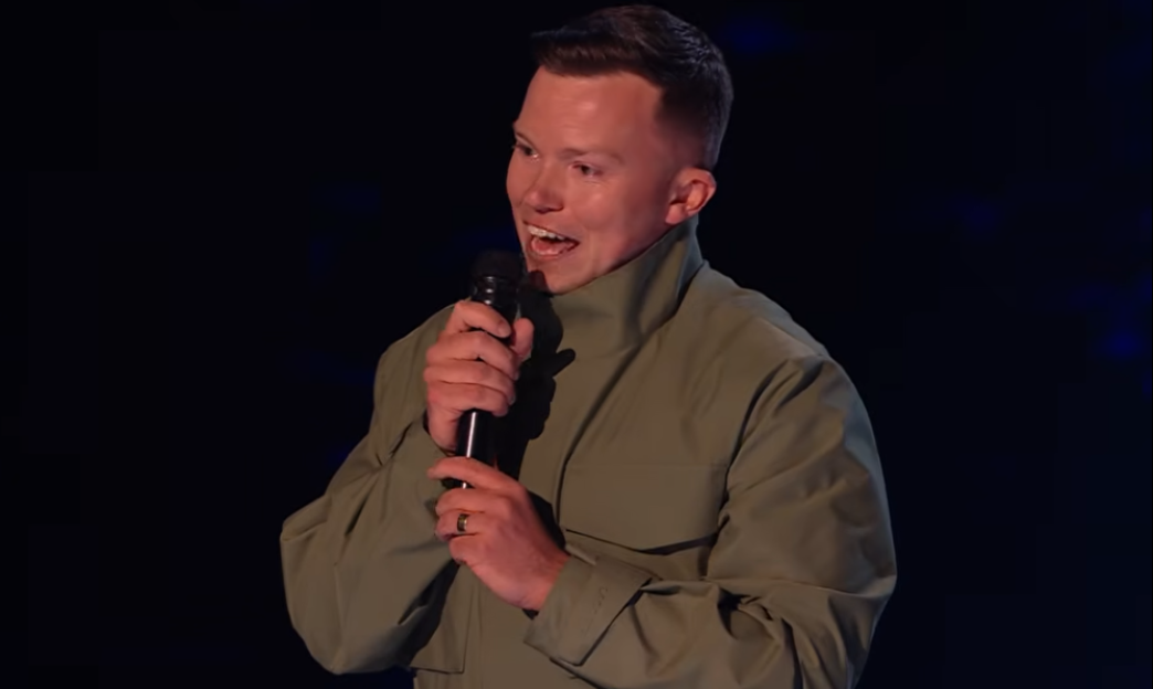 A man in a green shirt holds a microphone and sings.