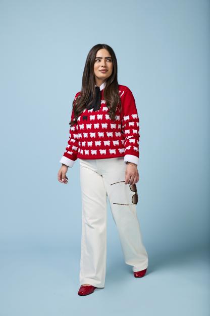 Emily Regan modeling a red sheep-patterned sweater, white trousers, and red ballet flats.