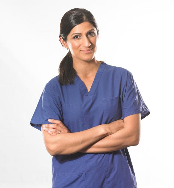 A female healthcare professional in blue scrubs with arms crossed, smiling.