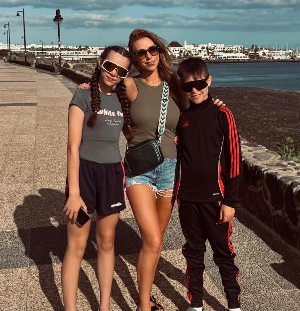 A woman and two children wearing sunglasses standing on a waterfront promenade.