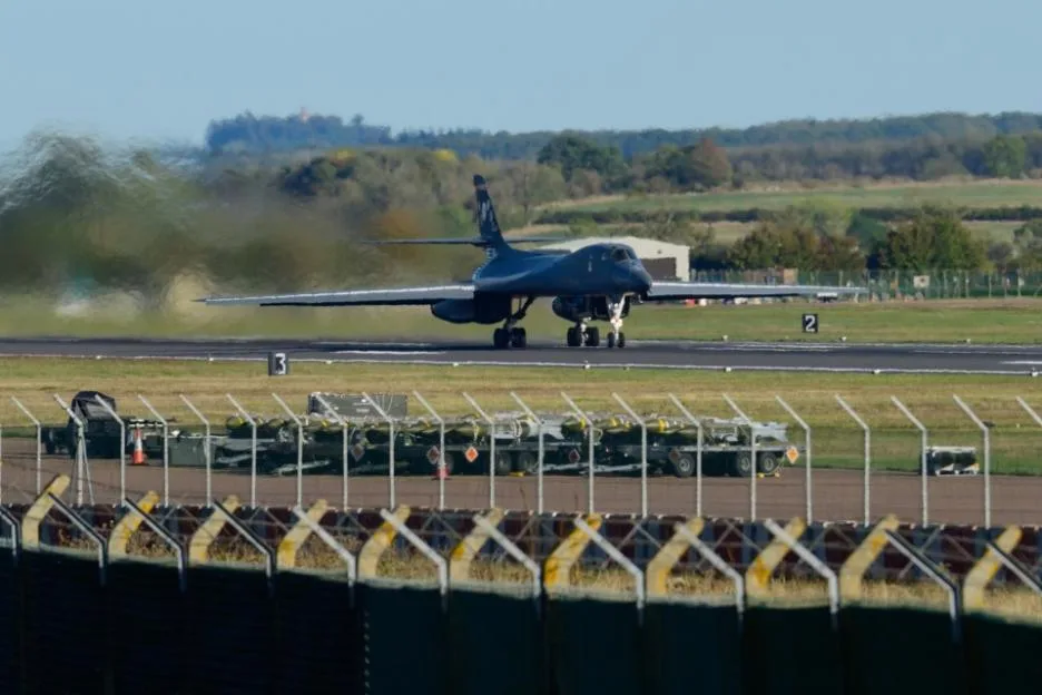 A Rockwell B1 Lancer heavy bomber prepares to depart from RAF Fairford, with munitions sitting on the tarmac nearby.